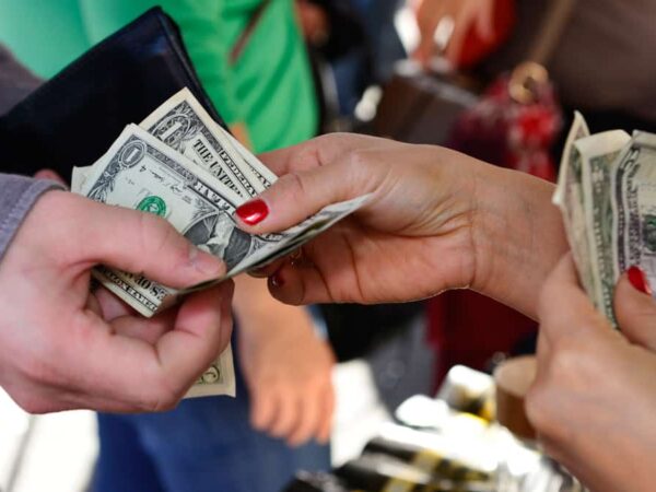One person's hands giving several dollar bills to another person's hand